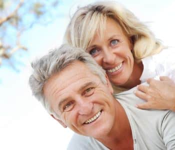 man and woman smiling with beautiful teeth after dental implant